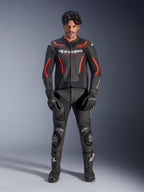 Männliches Model trägt die Alpinestars GP Force V2 Air Lederjacke in Schwarz und Red Fluo, mit perforierten Brusteinsätzen und weißem Branding, kombiniert mit schwarzer Motorrad-Lederhose, schwarzen Handschuhen und schwarzen Stiefeln für einen kompletten Racing-Look.