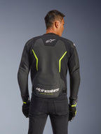 Blouson en cuir Alpinestars GP Force V2 Air, noir et jaune fluo, vue de dos d'un pilote montrant de larges panneaux en cuir perforé pour la circulation de l'air, marquage Alpinestars blanc et texte « Racing Ahead » jaune au bas du dos, équipement de moto sportif pour la route.
