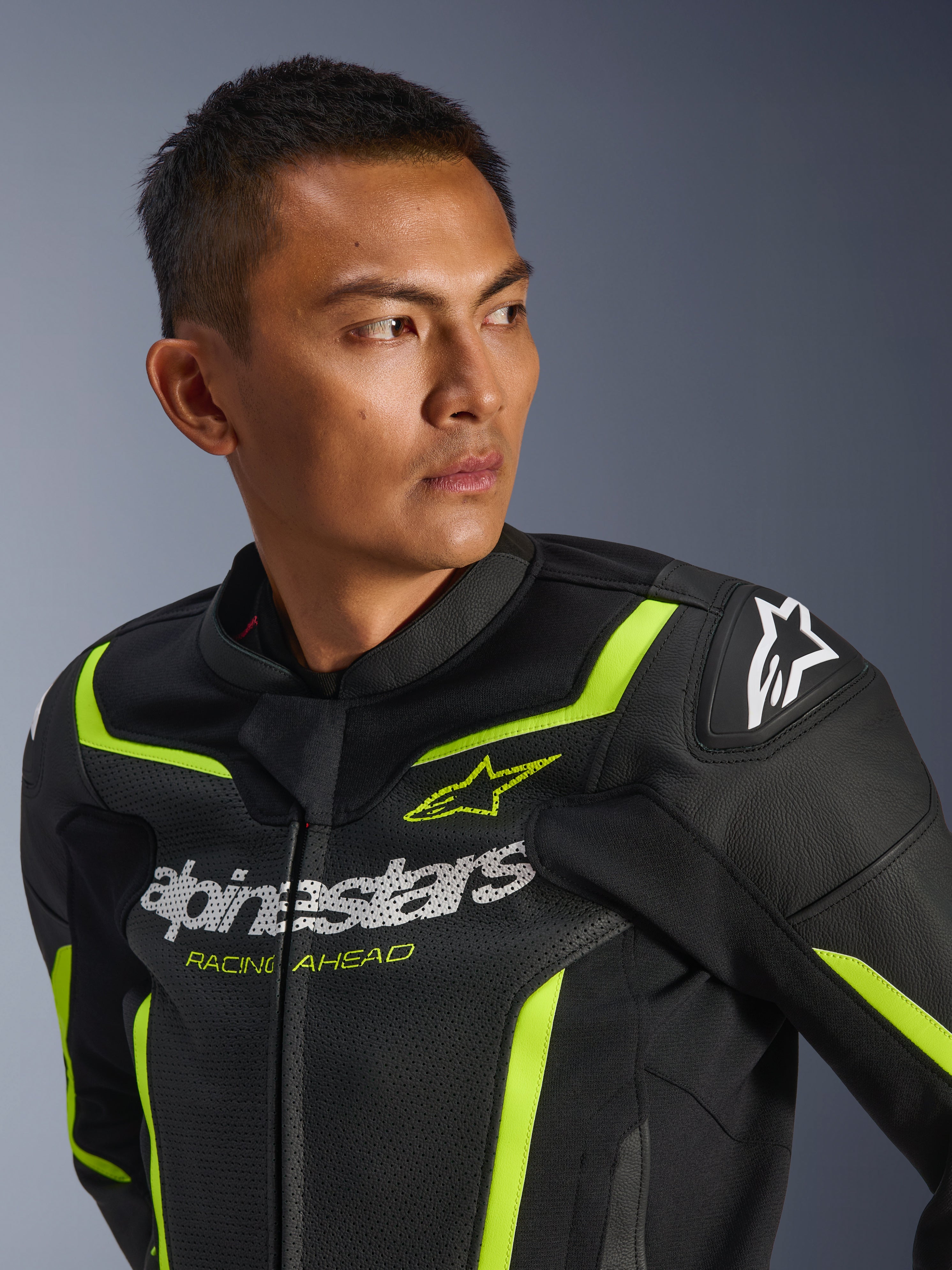 Veste en cuir Alpinestars GP Force V2 Air, noir et jaune fluo, veste de moto de sport perforée présentant un logo blanc sur la poitrine avec le texte 'Racing Ahead', des accents néon et des sliders de protection aux épaules, portée par un mannequin homme