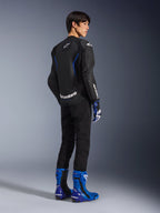 Modèle vu de dos portant le blouson en cuir Alpinestars GP Force V2 Airflow en Black Metallic Blue, doté de panneaux en cuir perforé et de logos blancs, associé à des gants de course assortis et des bottes bleues, équipement de moto sportif.