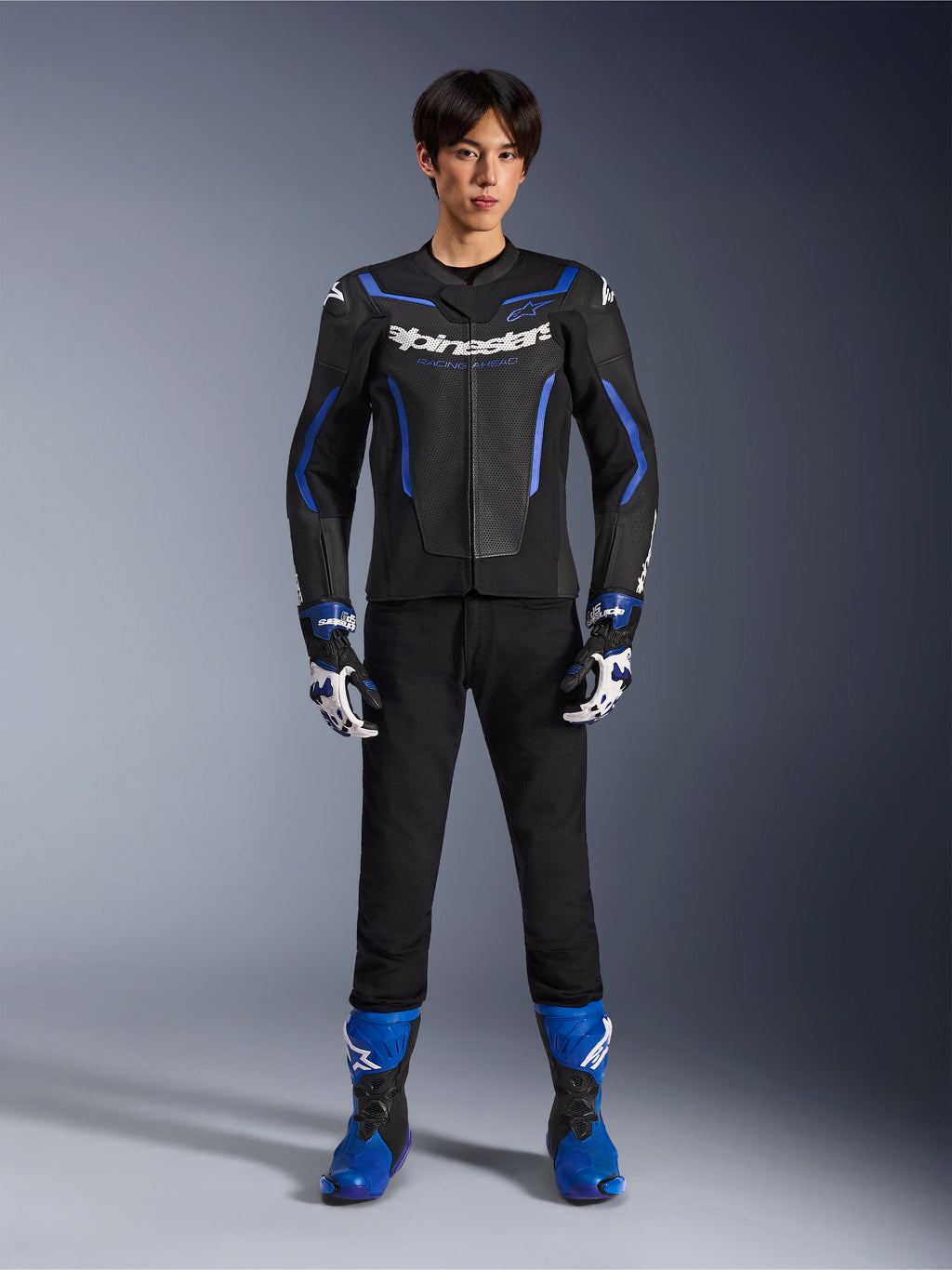 Blouson en cuir Alpinestars GP Force V2 Airflow en Noir Bleu Métallisé, porté avec des gants de course assortis, un pantalon noir et des bottes bleues, équipement professionnel de moto de sport, photo de studio en pied