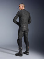 Alpinestars Dusk Lederjacke, Schwarz, rückseitige Dreiviertelansicht an einem Model, das eine passende Leder-Motorradhose und Performance-Rennstiefel trägt, mit Leder-Stretch-Akkordeon-Einsätzen, silbernem Alpinestars-Sternlogo am unteren Rücken und DUSK-Branding am oberen Rücken, professionelle Studioaufnahme
