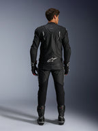 Alpinestars motorrijder van achteren gezien, Dusk Leather Jacket en Missile V3 Leather Pants, volledig zwart leren pak met witte accenten, jas met 'Dusk' branding en Alpinestars logo op de rug, gecombineerd met zwarte racelaarzen en handschoenen, gecoördineerde motorsport outfit voor wegraces