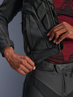 Alpinestars Dusk leren jas, zwart, close-up van de taille-verbindingsrits die wordt vastgemaakt aan een leren motorbroek, gedragen met een rood-zwarte basislaag met patroon, duurzame leren constructie voor rijden op de weg