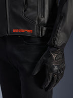 Blouson en cuir Alpinestars GP Plus V4, noir, gros plan sur le détail latéral avec marquage orange 'ADVANCED RACEWEAR ENGINEERING', boucle de réglage et gant de pilotage en cuir noir, vêtement de moto sport