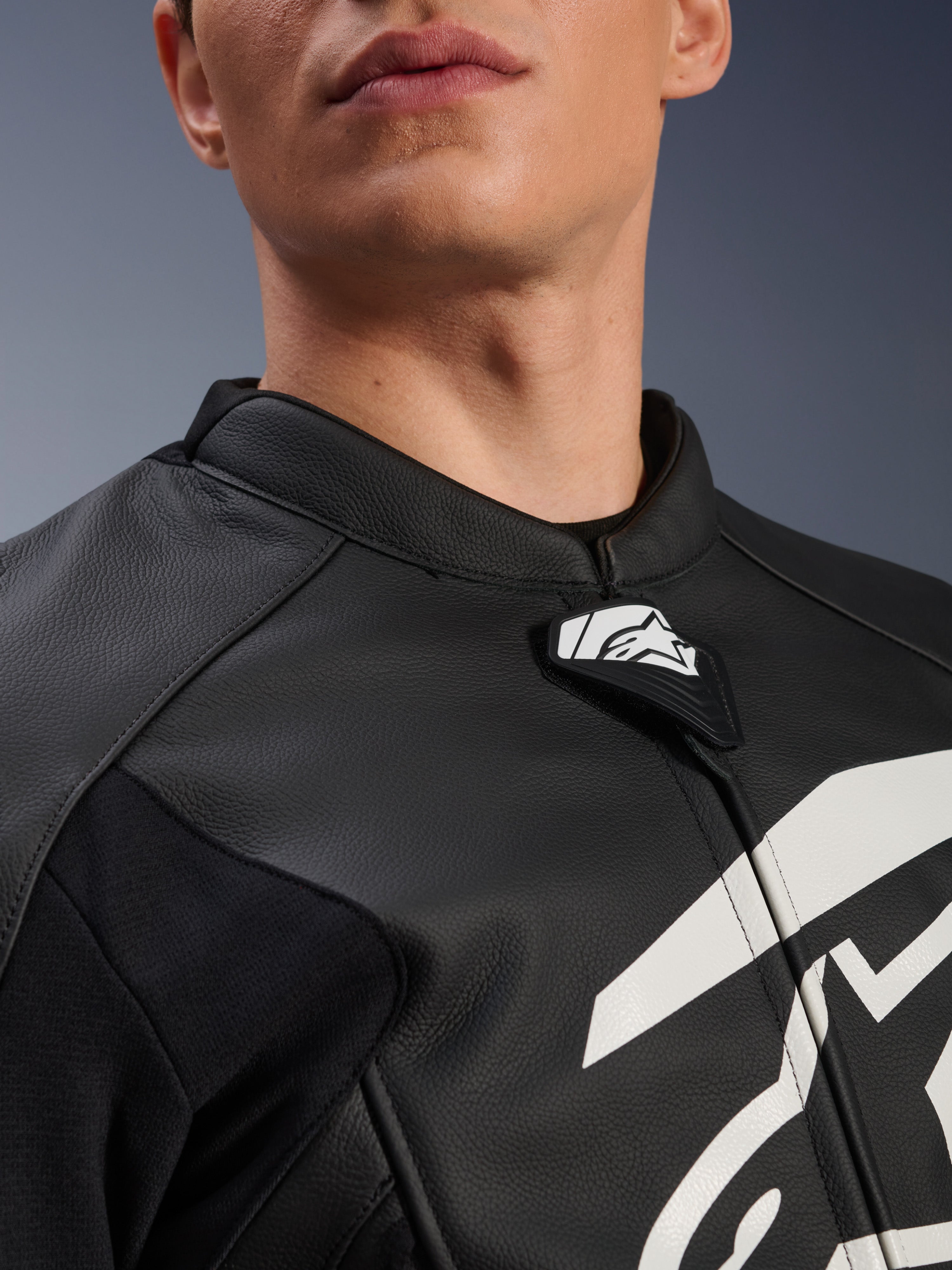 Blouson en cuir Alpinestars GP Plus V4, blouson de moto sport, noir et blanc, gros plan sur le col en cuir texturé et la languette du logo Alpinestars, graphique blanc sur la poitrine, design dérivé de la course