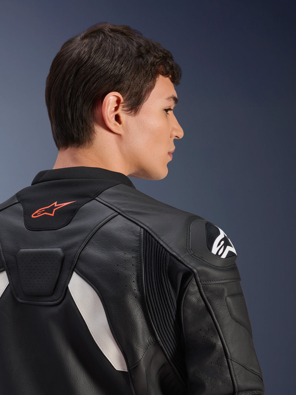 Blouson en cuir Alpinestars GP Plus V4, noir et blanc, vue arrière en gros plan d'un mannequin portant le blouson, avec logo rouge sur le col, protections d'épaules blanches et construction en cuir durable avec panneaux extensibles