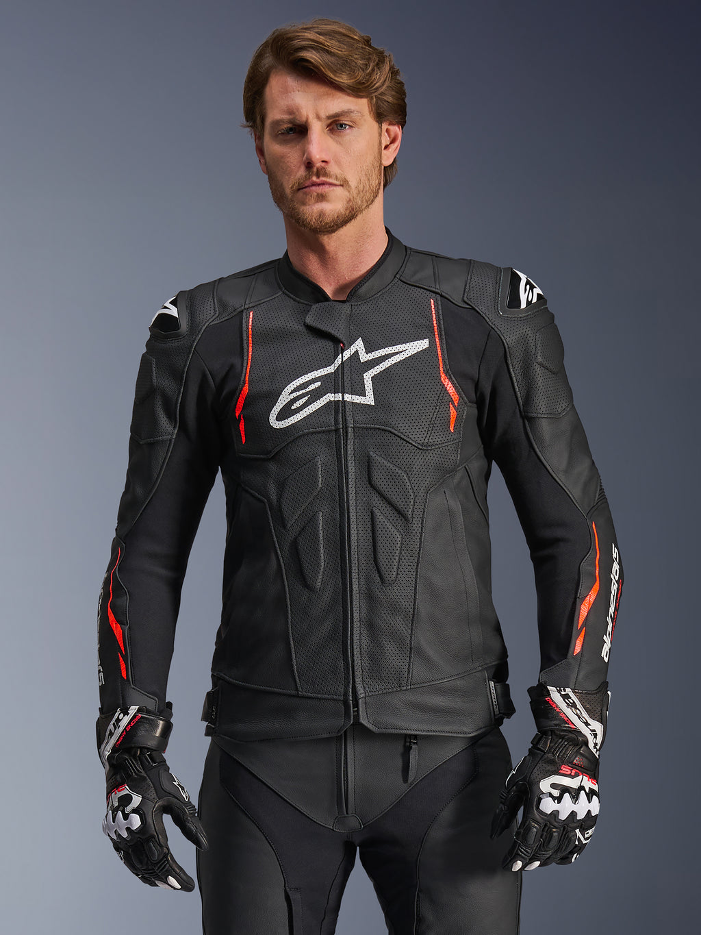 Veste en cuir Alpinestars Dusk Airflow, noire avec des accents rouge fluo et blancs, veste de moto de course en cuir, dotée de perforations étendues pour la ventilation, d'un logo blanc sur la poitrine et de sliders d'épaules externes, portée par un mannequin avec des gants de course assortis.