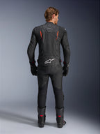 Veste en cuir Alpinestars Dusk Airflow, noir et rouge fluo, vue arrière montrant des perforations étendues et un grand logo blanc sur le bas du dos, portée avec un équipement de course en cuir assorti comprenant un pantalon, des bottes et des gants