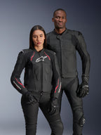 Alpinestars Stella Dusk Leather Jacket, Black Diva Pink White, worn by a female model alongside a male model in matching black leather gear, featuring pink and white accents, white star logo on chest, and black riding gloves
