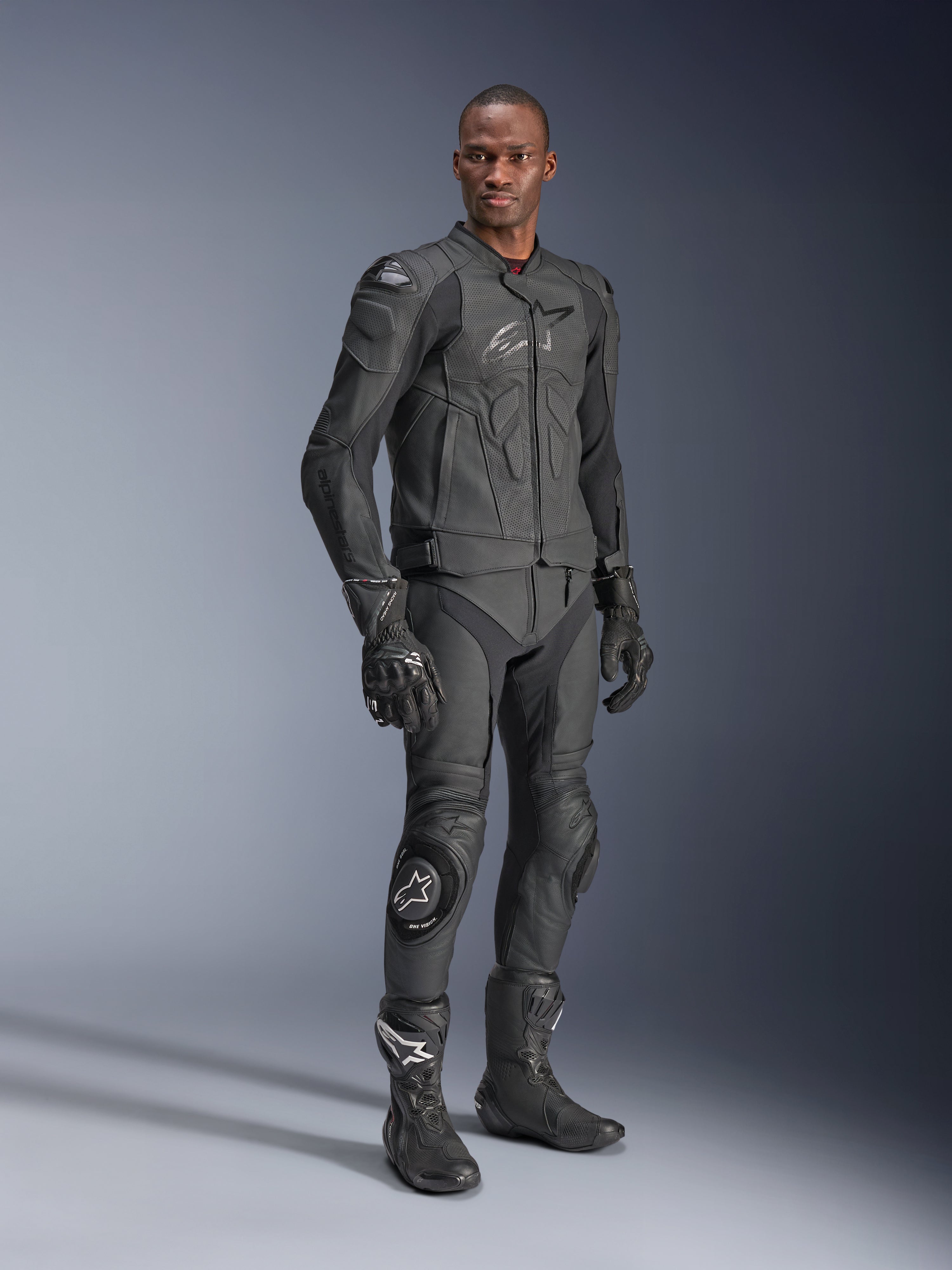 Alpinestars Dusk Airflow Leren Jas, Black Black, gedragen door een motorrijder in volledige technische uitrusting inclusief bijpassende leren broek, handschoenen en laarzen, voorzien van geperforeerde leren panelen voor ventilatie en geïntegreerde bescherming voor sportief motorrijden