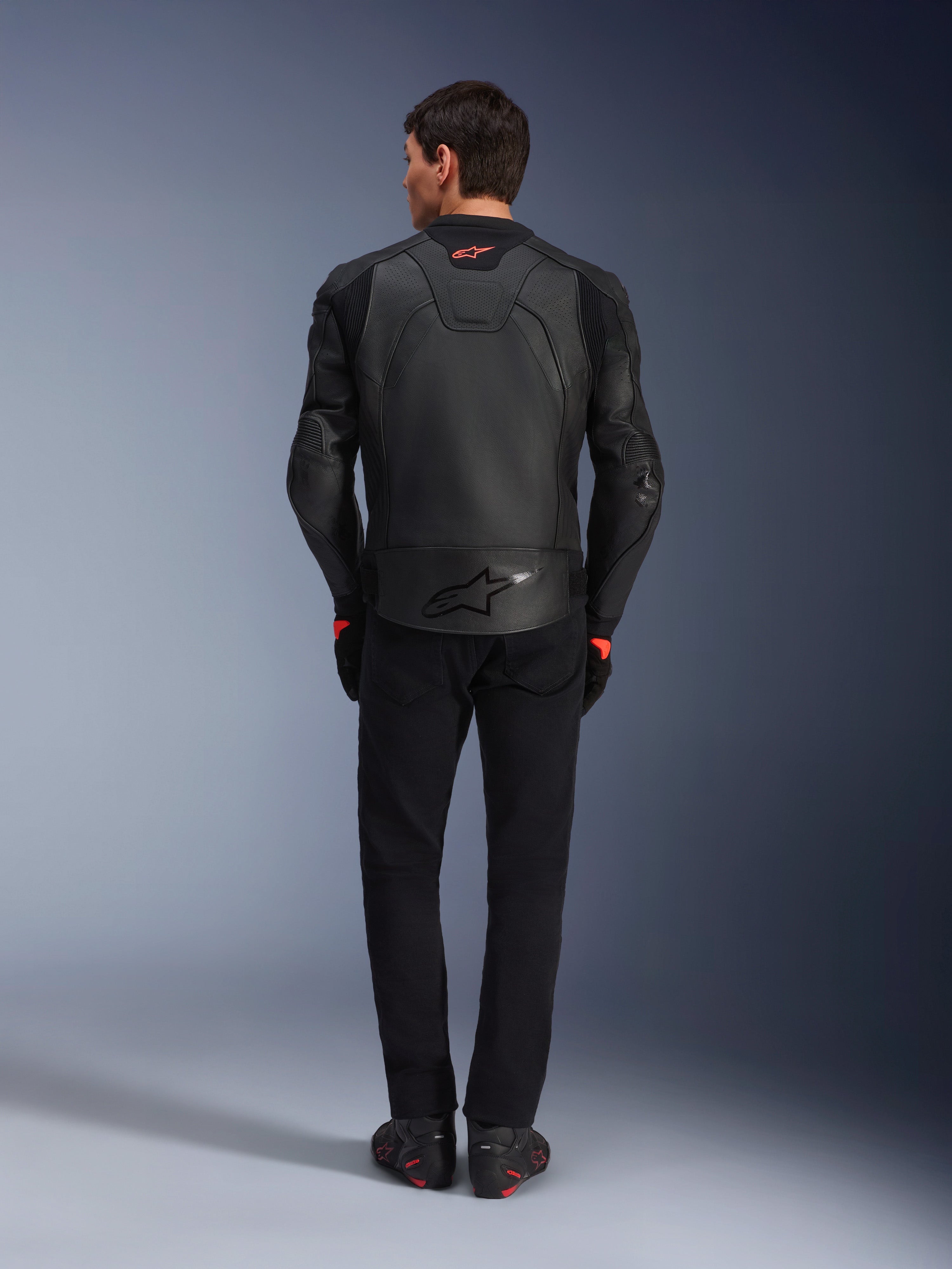 Alpinestars GP Plus R V4 Airflow Lederjacke, Schwarz, Rückansicht eines Fahrers in kompletter Ausrüstung, mit perforiertem Leder für Belüftung und roten Logo-Akzenten, schlankes Sport-Fit-Design, kombiniert mit schwarzer Hose und Motorradstiefeln