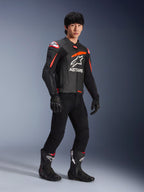 Männlicher Fahrer in der Alpinestars GP Plus R V4 Airflow Lederjacke, Schwarz mit Red Fluo und weißen Akzenten, mit perforiertem Leder und ASTARS-Brustlogo, getragen mit schwarzer Motorradhose und schwarzen Motorradstiefeln, sportliche Performance-Ausrüstung