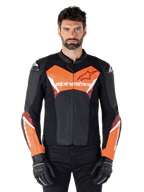 Alpinestars Faster V3 Lederjacke, Sport-Motorradjacke, Schwarz und Rot Fluo, getragen von einem männlichen Model mit schwarzen Motorradhandschuhen und -hosen, mit markantem Alpinestars-Branding auf Brust und Unterarmen, hochwertige Lederkonstruktion für den Straßeneinsatz.