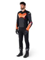Männlicher Fahrer in der Alpinestars Faster V3 Lederjacke in Schwarz und Rot Fluo, kombiniert mit schwarzer Motorradhose, Handschuhen und Stiefeln. Die Jacke zeichnet sich durch eine vom Rennsport abgeleitete Silhouette mit markanten fluoreszierenden roten Akzenten an Brust und Ärmeln, weißem Alpinestars-Branding und einer hochwertigen Lederkonstruktion aus.
