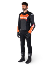 Mannelijke motorrijder die de Alpinestars Faster V3 Leren Jas draagt in Black Red Fluo, gecombineerd met een zwarte motorbroek, handschoenen en laarzen. De jas heeft een op de racerij geïnspireerd silhouet met opvallende fluorescerend rode accenten op de borst en mouwen, witte Alpinestars-branding en een hoogwaardige lederen constructie.