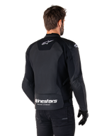 Alpinestars Faster V3 Lederjacke, Schwarz und Weiß, Rückansicht an einem Fahrer, mit weißem Stern-Logo auf dem oberen Rücken und großem Alpinestars-Branding mit „Racing Ahead“ am unteren Abschluss, verlängerte Rückseite für bessere Abdeckung beim Fahren, hochwertige Sport-Lederkonstruktion