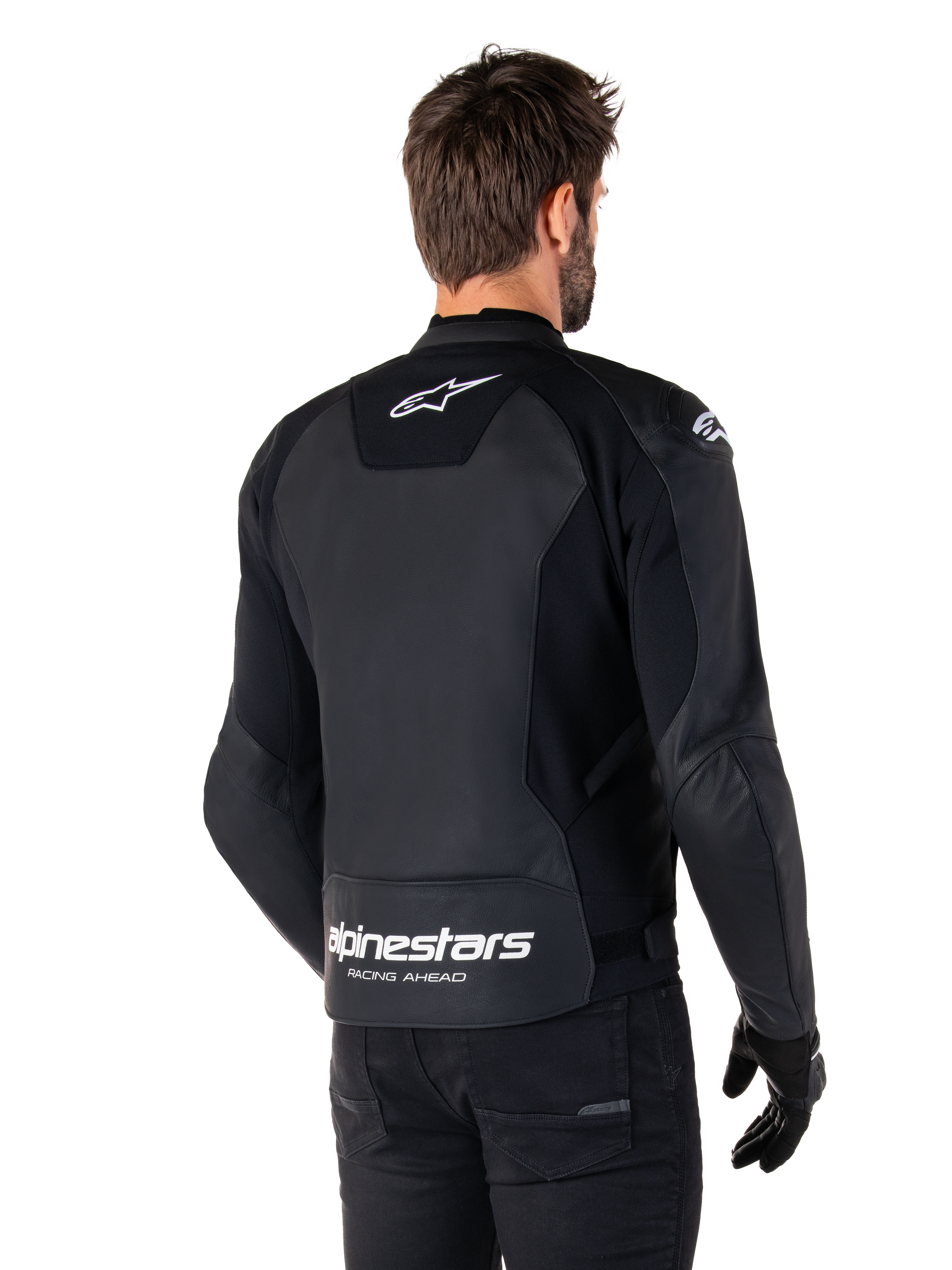 Alpinestars Faster V3 Lederjacke, Schwarz und Weiß, Rückansicht an einem Fahrer, mit weißem Stern-Logo auf dem oberen Rücken und großem Alpinestars-Branding mit „Racing Ahead“ am unteren Abschluss, verlängerte Rückseite für bessere Abdeckung beim Fahren, hochwertige Sport-Lederkonstruktion