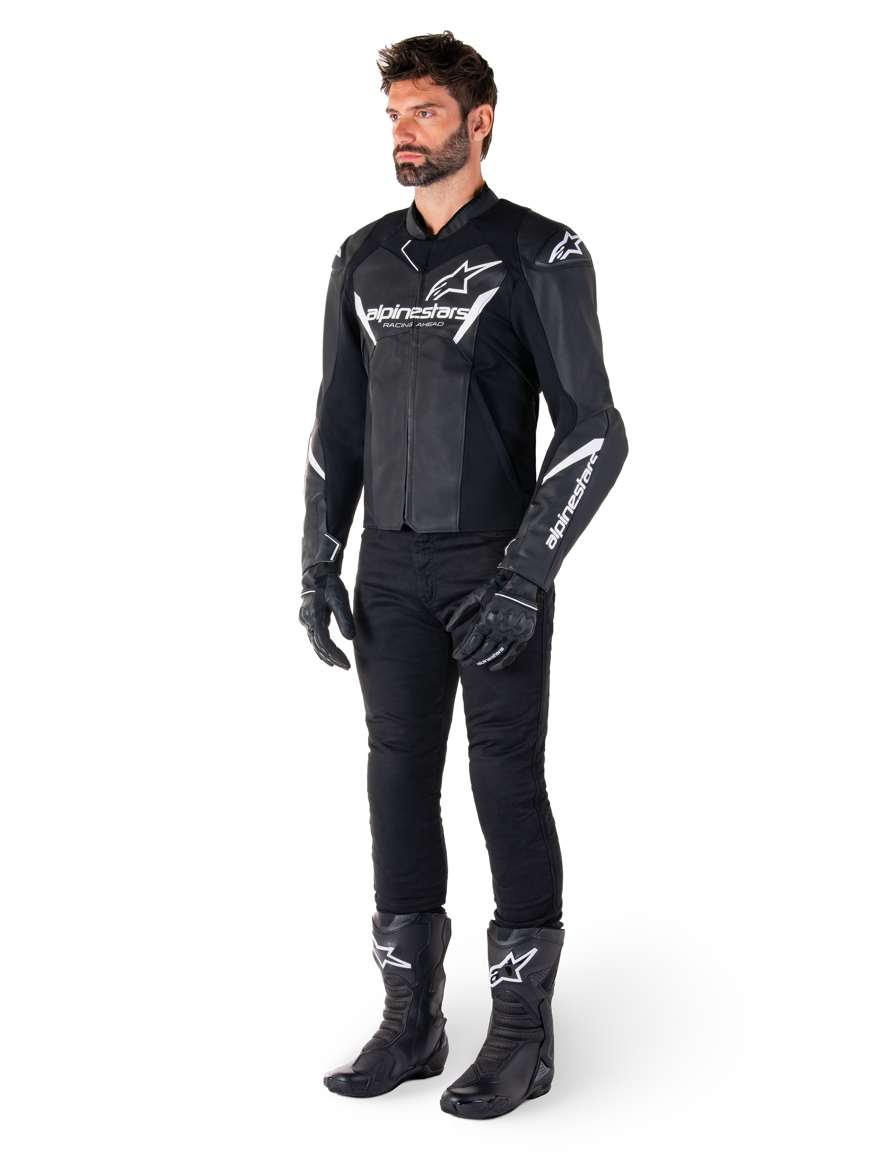 Männliches Modell in Alpinestars Faster V3 Lederjacke, Sport-Motorradjacke, Schwarz und Weiß, kombiniert mit schwarzer Motorradhose, Handschuhen und Stiefeln, mit weißen Brandings und Logos, sportliche Silhouette für den Straßenrennsport