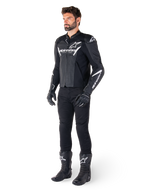 Modèle portant une veste en cuir Alpinestars Faster V3 Airflow, noir et blanc, avec cuir perforé et logos Alpinestars blancs, associée à un pantalon, des gants et des bottes de moto noirs, équipement de moto de sport