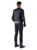 Veste en cuir Alpinestars Faster V3 Airflow, noir et blanc, vue arrière montrant les panneaux en cuir perforé et le logo Alpinestars distinctif sur le bas du dos, portée par un pilote avec un pantalon de moto, des gants et des bottes noirs.