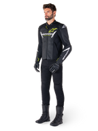 Motard portant la veste en cuir Alpinestars Faster V3 Airflow en noir, blanc et jaune fluo, avec pantalon et bottes de moto noirs, présentant des panneaux en cuir perforé, des logos blancs et des touches jaune fluo, équipement de pilotage sportif professionnel