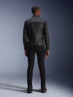 Veste en cuir Alpinestars Blacktrack, vue arrière, cuir de bovin premium noir, dotée de panneaux en accordéon sur les omoplates pour la mobilité, portée avec un pantalon slim noir et des bottes noires, équipement de moto urbain contemporain.