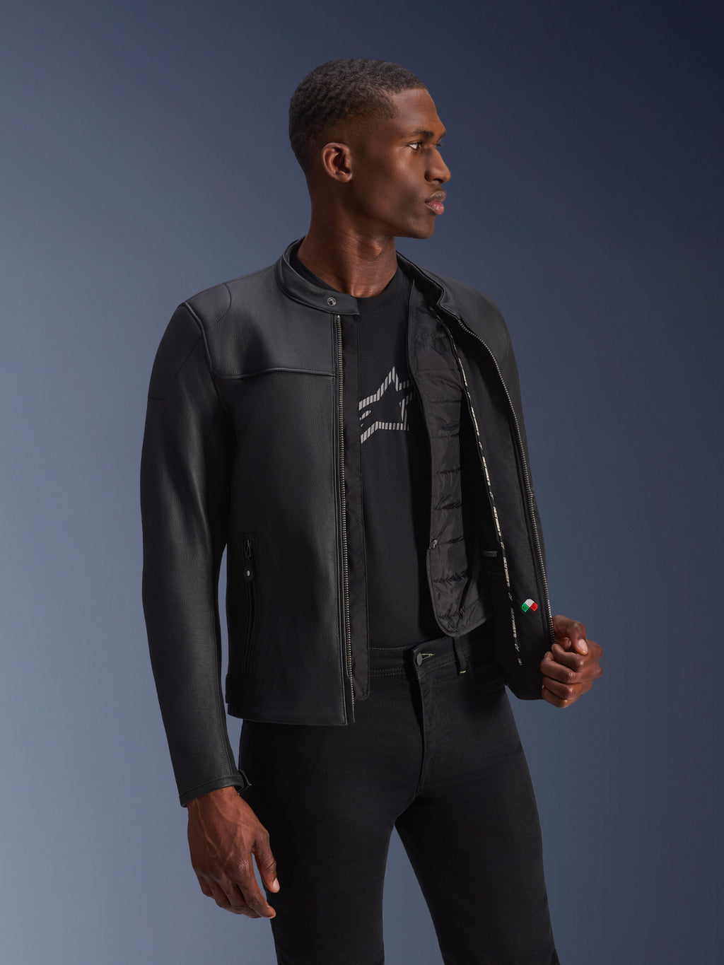Veste en cuir Alpinestars Blacktrack, noir, cuir de bovin de première qualité avec une coupe sur mesure, ouverte montrant le gilet thermique détachable et les détails intérieurs, portée par un mannequin, équipement de moto urbain moderne