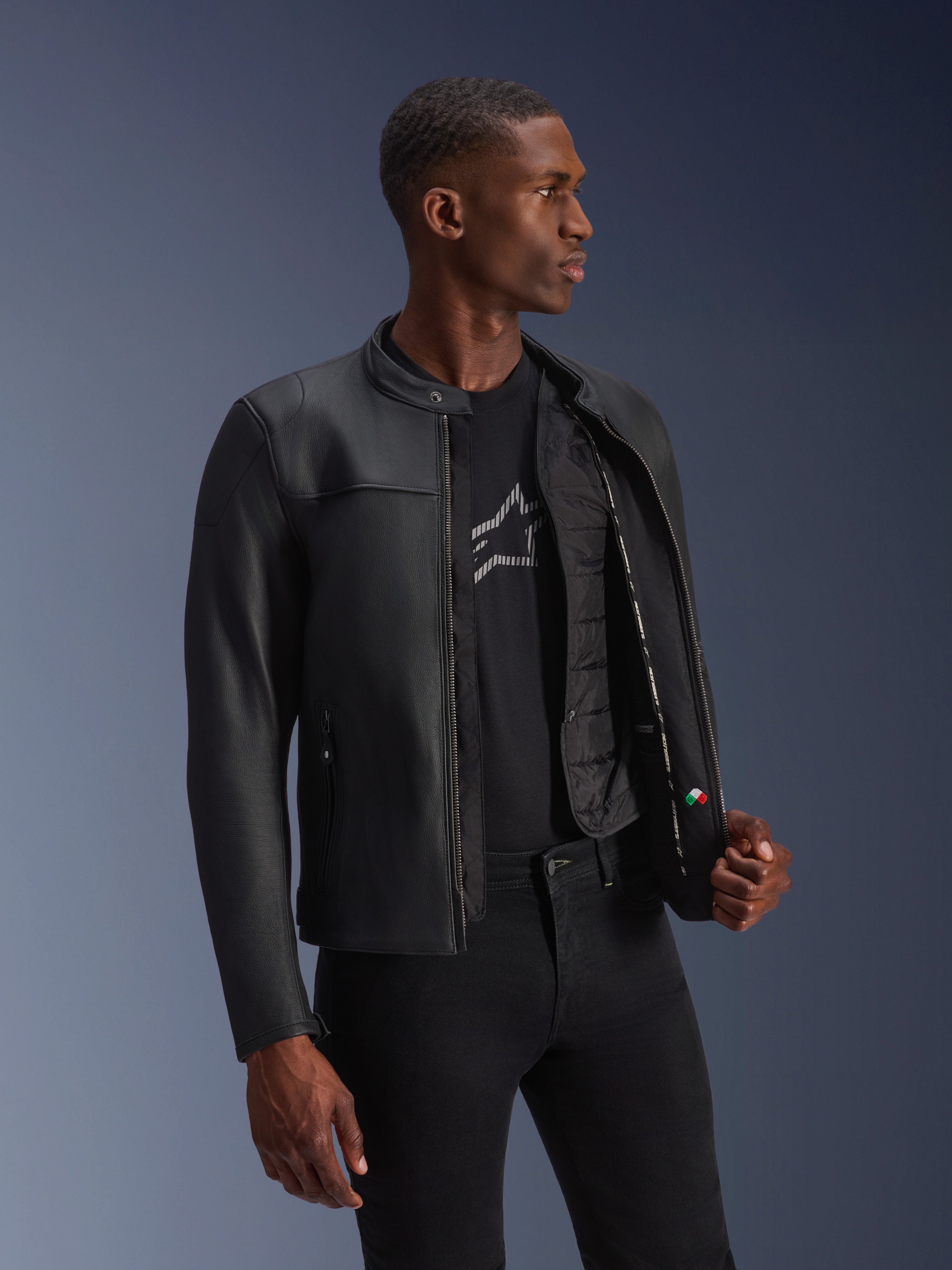 Veste en cuir Alpinestars Blacktrack, noir, cuir de bovin de première qualité avec une coupe sur mesure, ouverte montrant le gilet thermique détachable et les détails intérieurs, portée par un mannequin, équipement de moto urbain moderne