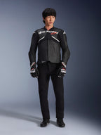 Model draagt de Alpinestars Atem V5 leren jas in zwart en wit, voorzien van witte Alpinestars-branding en een rood ster-logo op de borst, gecombineerd met een zwarte broek en zwart-witte racehandschoenen, strakke performance motoruitrusting