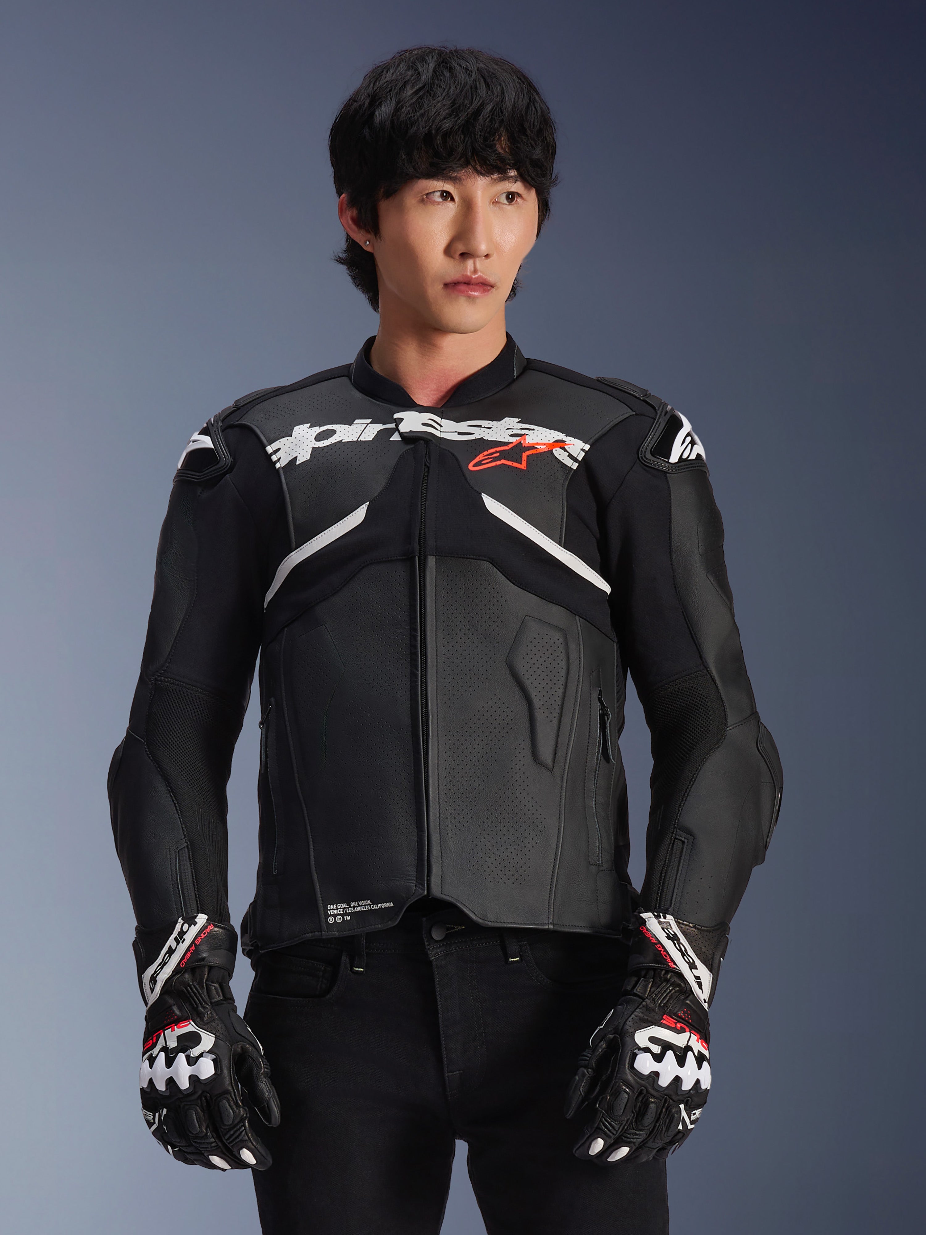 Alpinestars Atem V5 leren motorjas, motorracejas, zwart met witte en rode accenten, hoogwaardige leren constructie met bepantserde bescherming, gedragen met bijpassende racehandschoenen