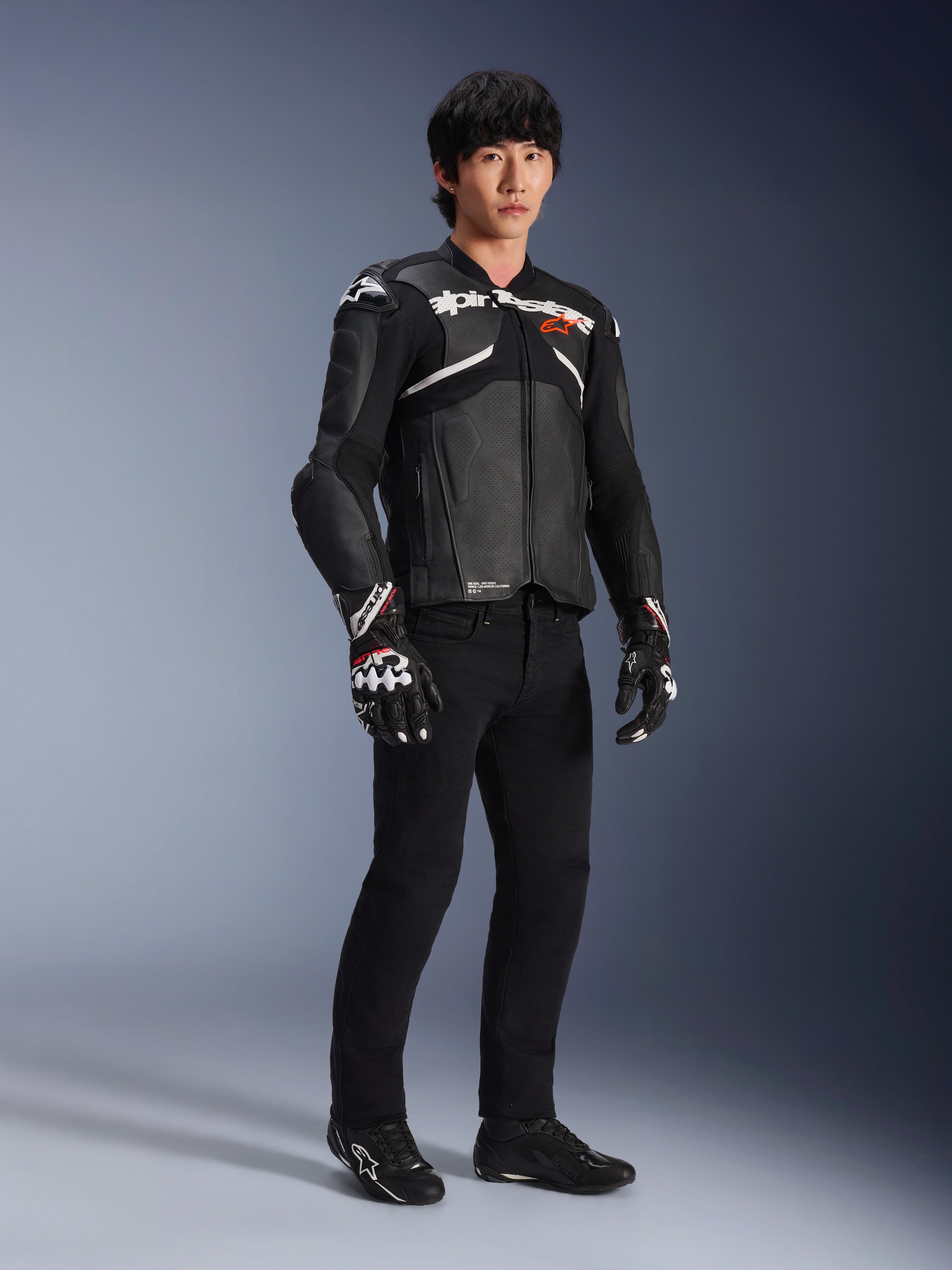 Alpinestars Atem V5 Leren Jas, motorracejas, zwart en wit, gedragen met een zwarte broek en bijpassende handschoenen, met witte Alpinestars-branding op de borst en beschermende schouderprotectie.