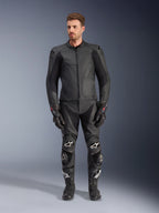 Alpinestars Caliber Leren Jas, zwart motorjack, gedragen met bijpassende racebroek, handschoenen en laarzen, voorzien van een strak ontwerp met ton-sur-ton logo's, stretchpanelen op de mouwen en beschermende schoudersliders, professionele studio-opname