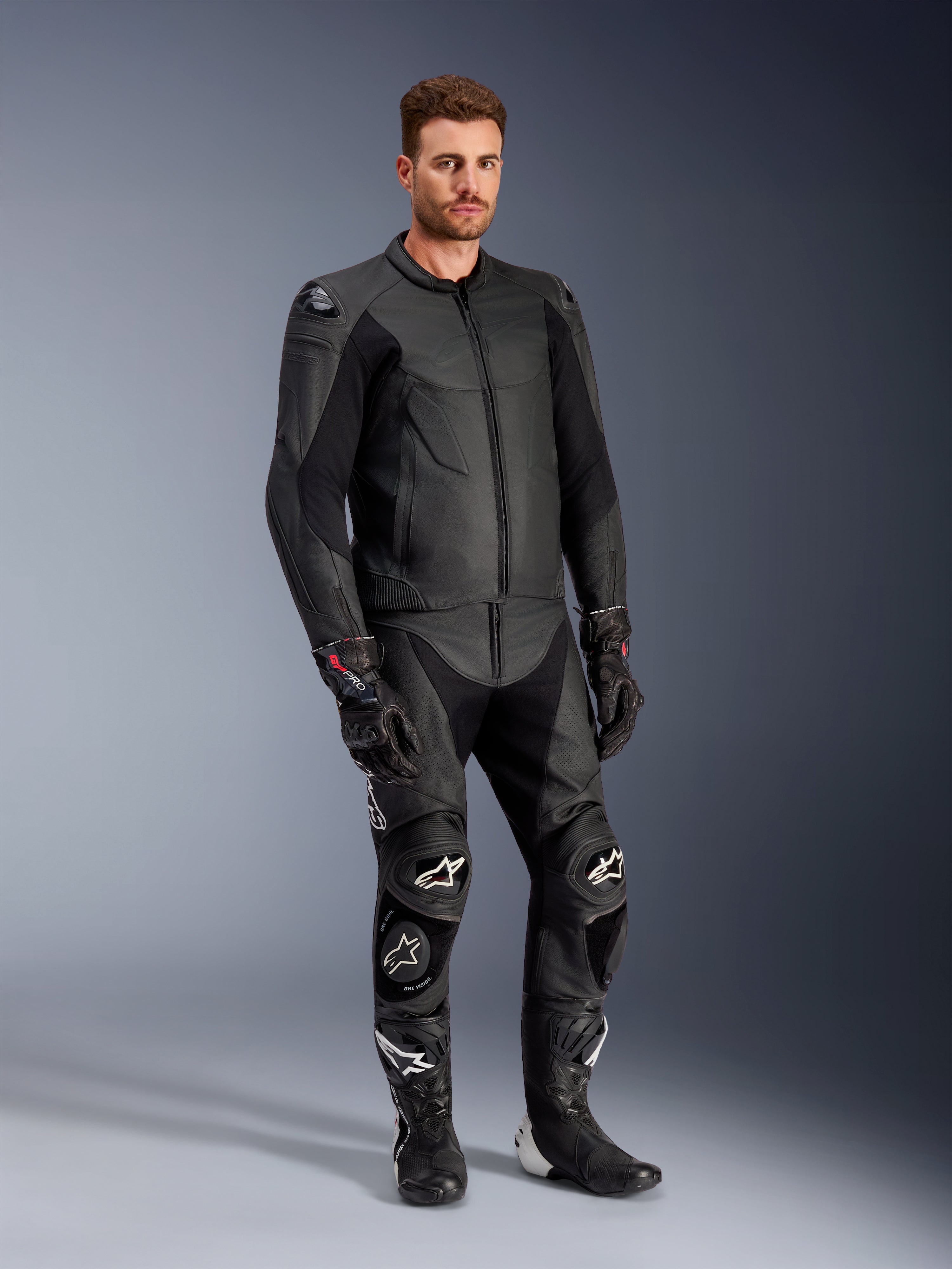 Alpinestars Caliber leren jas in het zwart, gecombineerd met bijpassende zwarte leren motorbroek, racehandschoenen en laarzen, mannelijk model in een complete sportieve weguitrusting