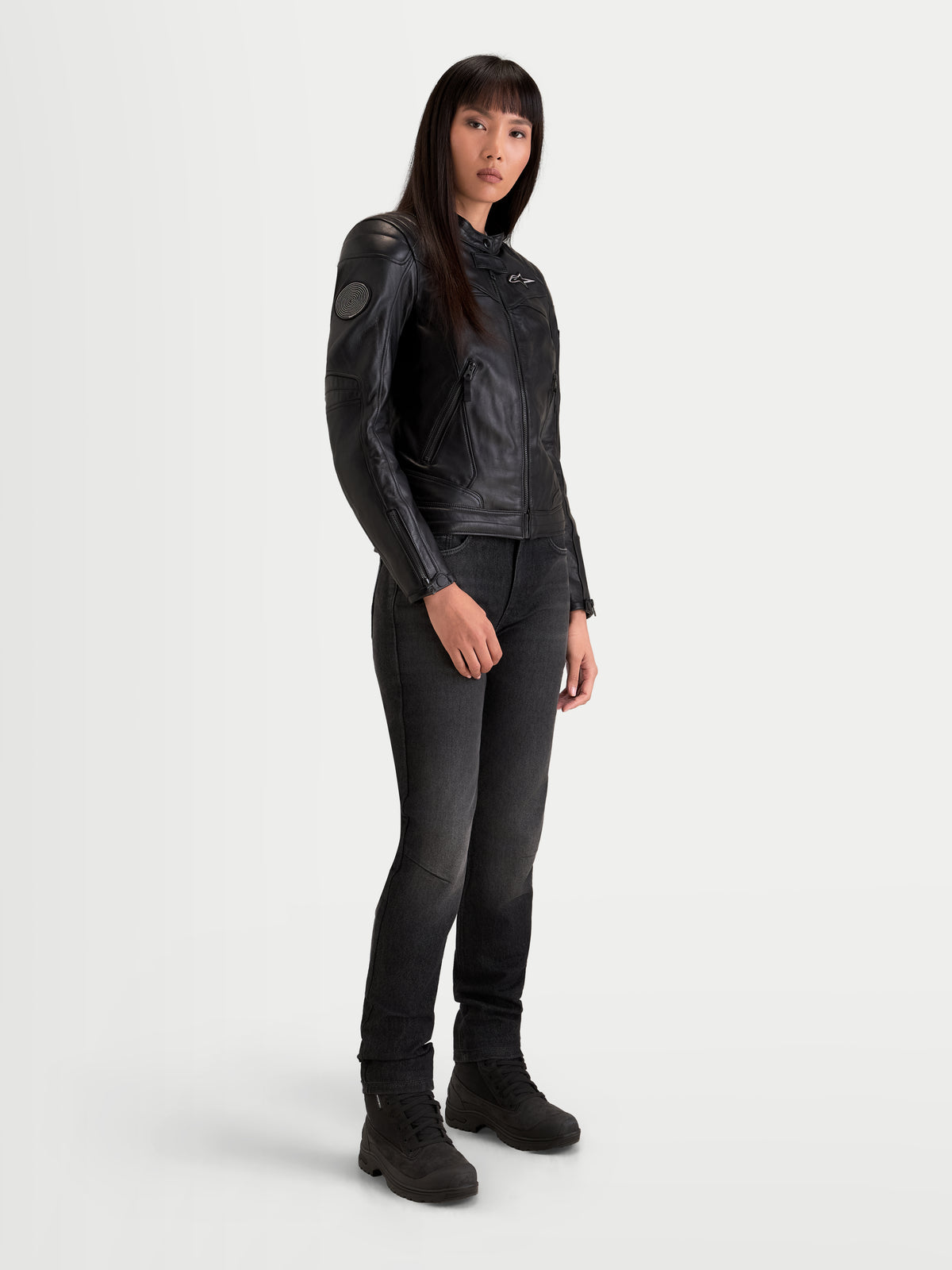 Alpinestars Revea Veste en cuir pour femme, veste de moto urbaine contemporaine noire, vue de trois quarts sur un modèle portant un jean foncé et des bottes