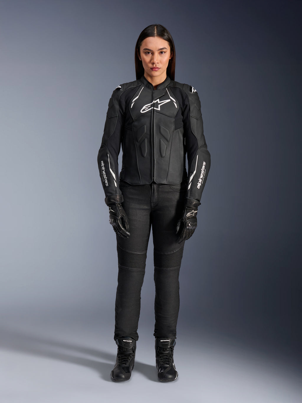 Alpinestars Stella Dusk leren damesjas, zwart en wit, gedragen door een model met bijpassende zwarte broek en laarzen, vooraanzicht, witte Alpinestars logo's op de borst en mouwen, premium runderleren beschermende kleding voor dames