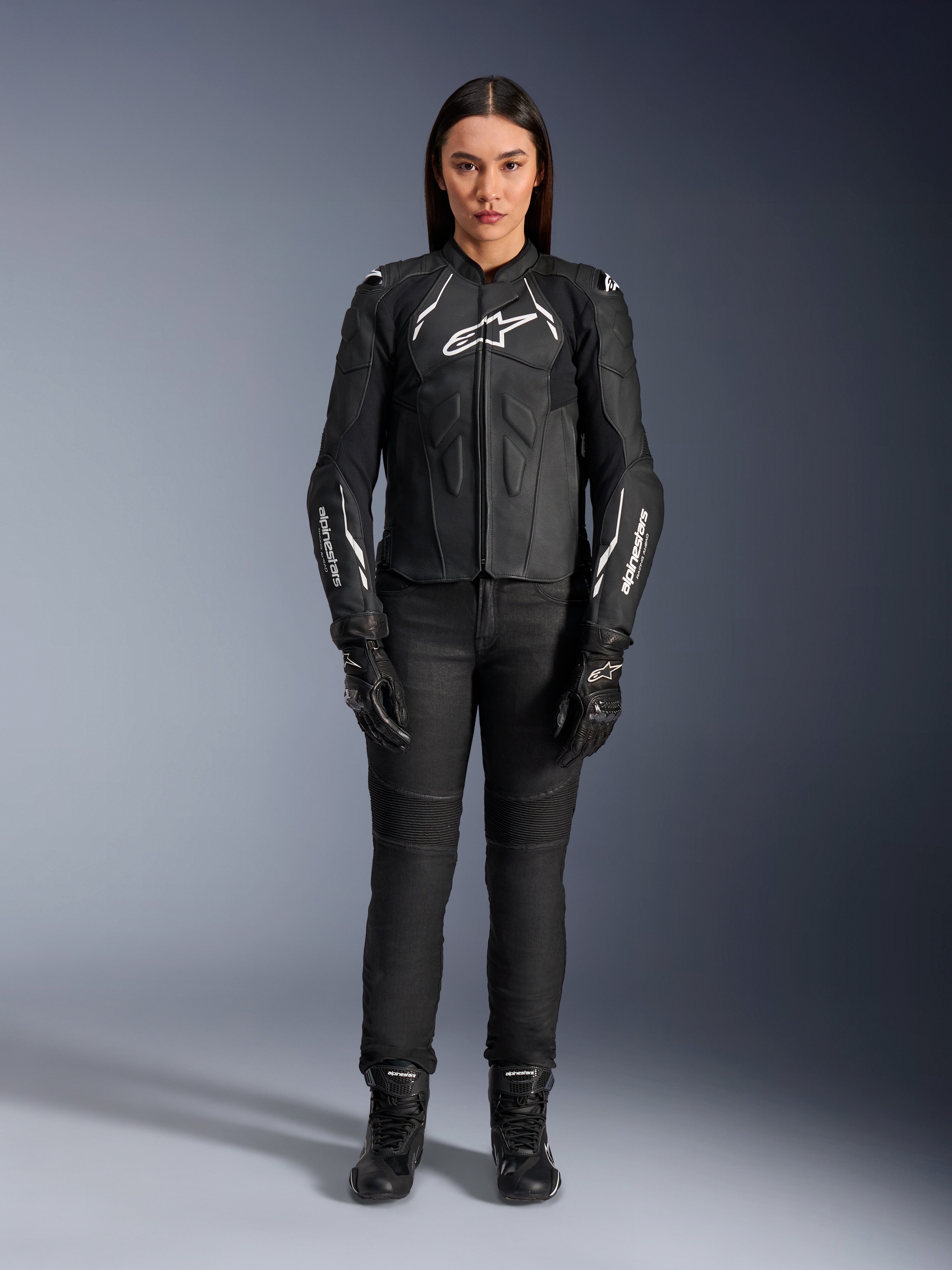 Alpinestars Stella Dusk leren damesjas, zwart en wit, gedragen door een model met bijpassende zwarte broek en laarzen, vooraanzicht, witte Alpinestars logo's op de borst en mouwen, premium runderleren beschermende kleding voor dames