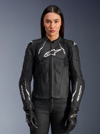 Alpinestars Stella Dusk lederen jas, dames motorjas, zwart met witte accenten, hoogwaardige lederen constructie, gevoerde borst- en schouderbescherming, ritssluiting aan de voorzijde, vrouwelijk model draagt de jas met zwarte motorhandschoenen