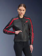 Alpinestars Stella Dyno leren jas, dames motorjas, zwart met rood, gedragen door een model met zwarte jeans, rode racing strepen op de schouders en mouwen met opvallende branding, hoogwaardige leren constructie, op erfgoed geïnspireerd ontwerp voor stedelijke ritten