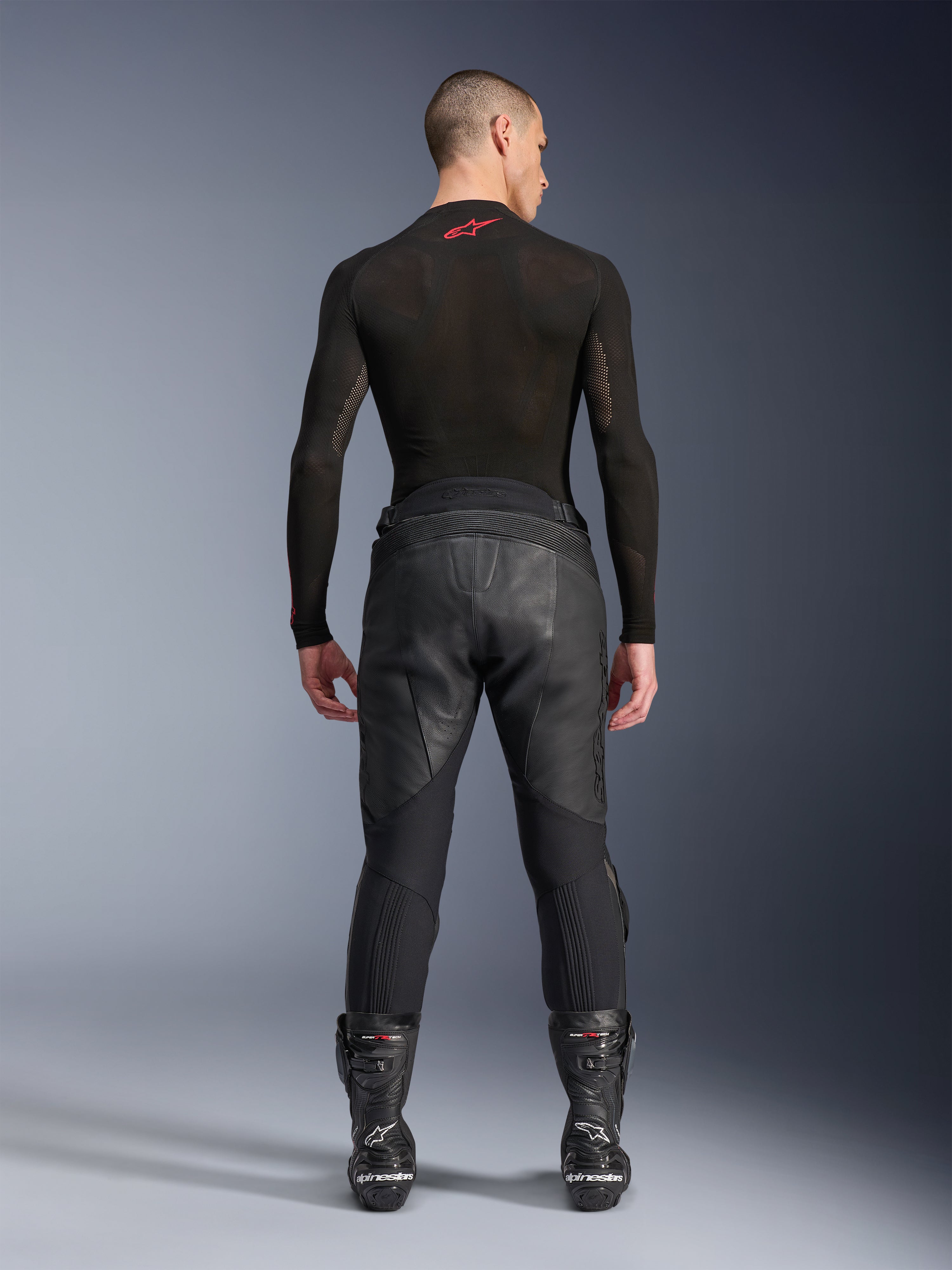Alpinestars Missile V3 Leren Broek, zwart, achteraanzicht op model die een zwart compressieshirt met lange mouwen en racelaarzen draagt, premium leren constructie met hoge taille overlap en stretchzones, professionele motorrace-uitrusting