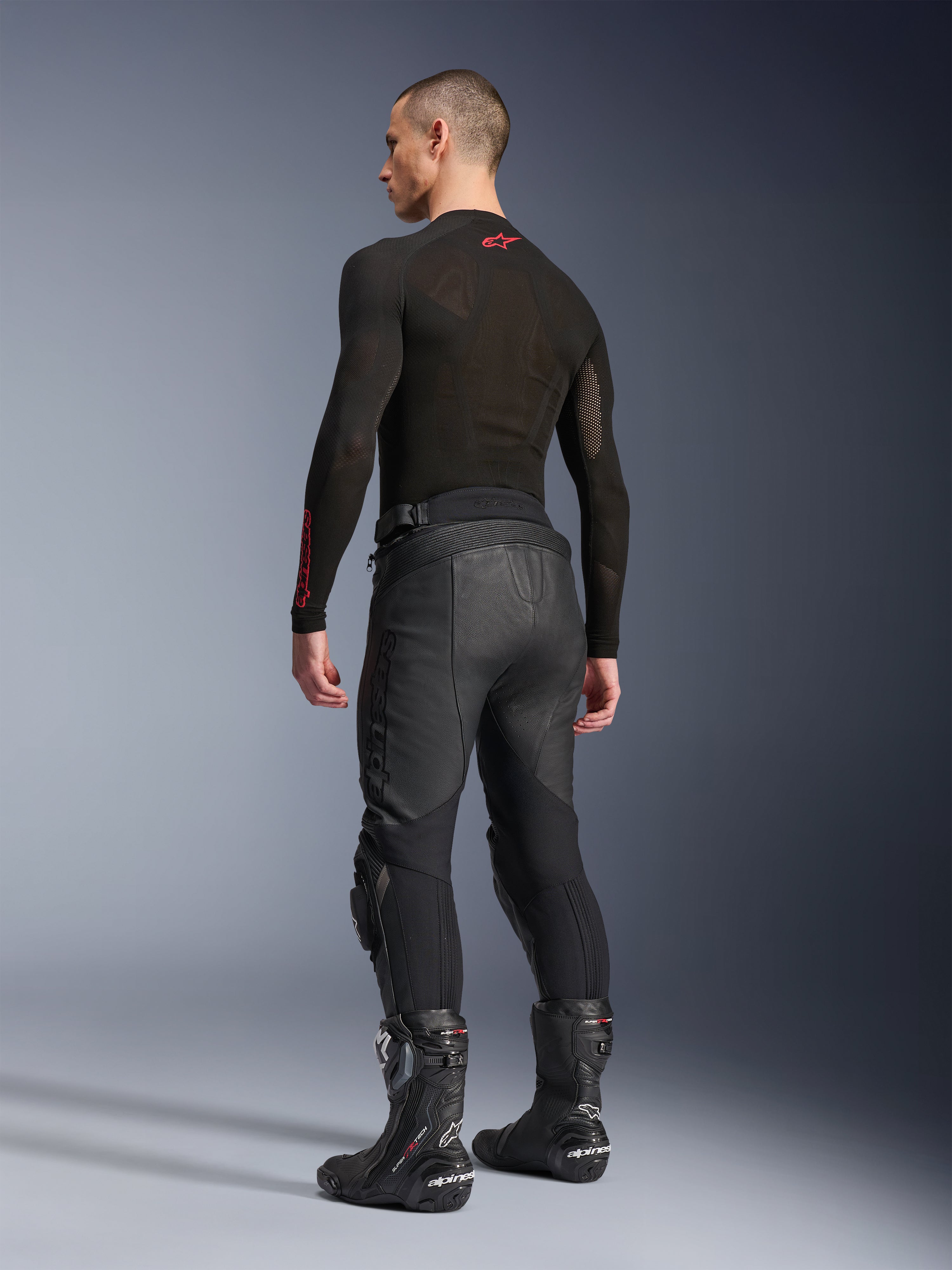 Alpinestars Missile V3 Leren Broek, zwart, achteraanzicht op model, gedragen met een zwarte basislaag en zwarte motorlaarzen, met accordeon lederen stretchpanelen en een voorgevormd ontwerp voor een ergonomische pasvorm.