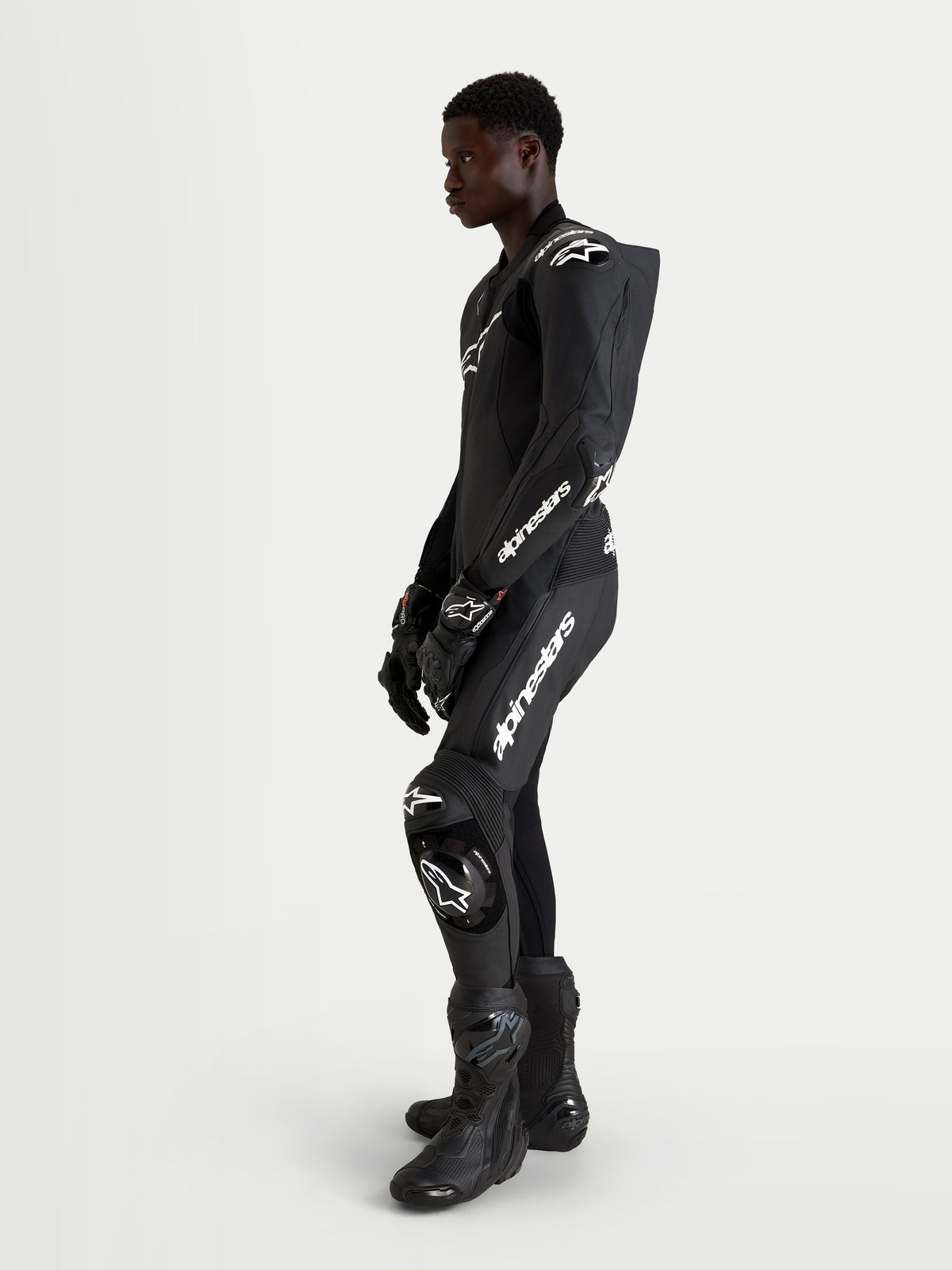 Alpinestars Missile V3 Leather Suit - 1 Piece, combinaison en cuir noire pour la course moto, avec détails de logos blancs, bosse aérodynamique et protections, vue de profil avec un modèle