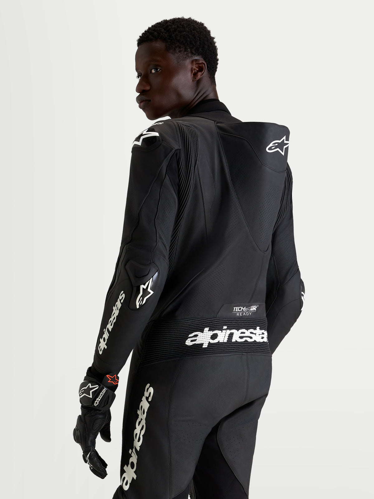 Combinaison en cuir Missile V 3 1 Pc d'Alpinestars, combinaison moto noire pour homme, vue de dos montrant la bosse aérodynamique, les protections d'épaules et le marquage blanc