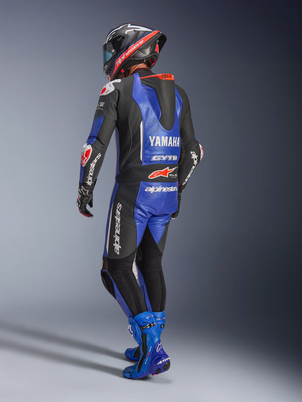 Alpinestars Yamaha GP-R7 Einteiliger Lederanzug, Metallic-Blau, Schwarz und Weiß, Rückansicht mit aerodynamischem Rennhöcker und Yamaha-Branding, getragen mit passenden blauen Rennstiefeln und Helm, professioneller Performance-Lederanzug für den Rennsport