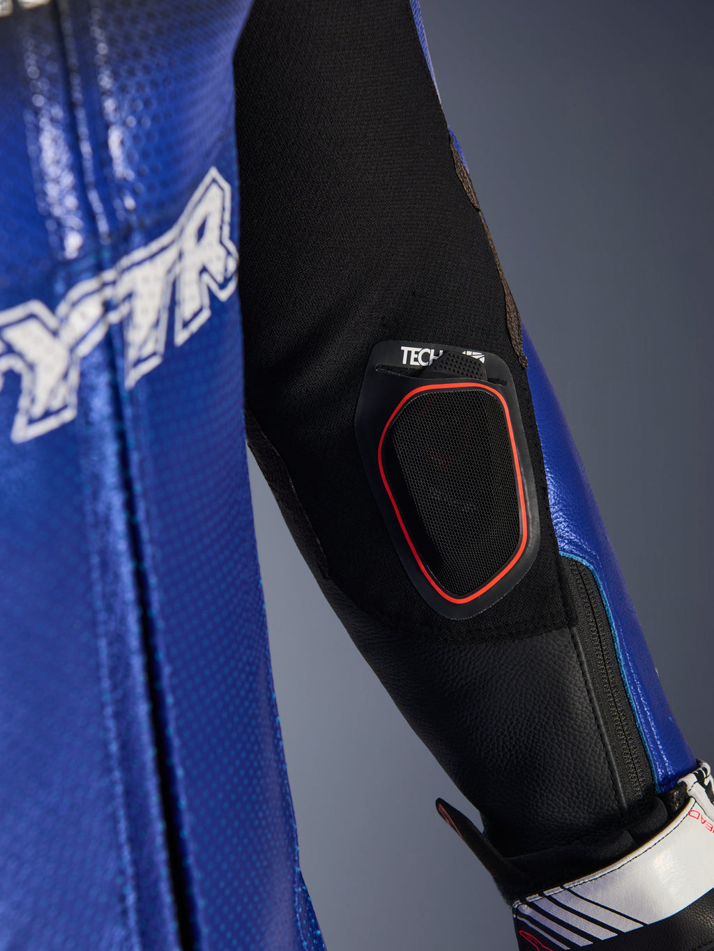 Nahaufnahme des Unterarms des Yamaha GP-R7 Einteiligen Lederanzugs, mit integrierter Tech-Air 10 Bluetooth-Displaytasche mit rotem Rand, metallic-blauem, perforiertem Leder und schwarzen Stretch-Gewebeeinsätzen für Rennperformance.