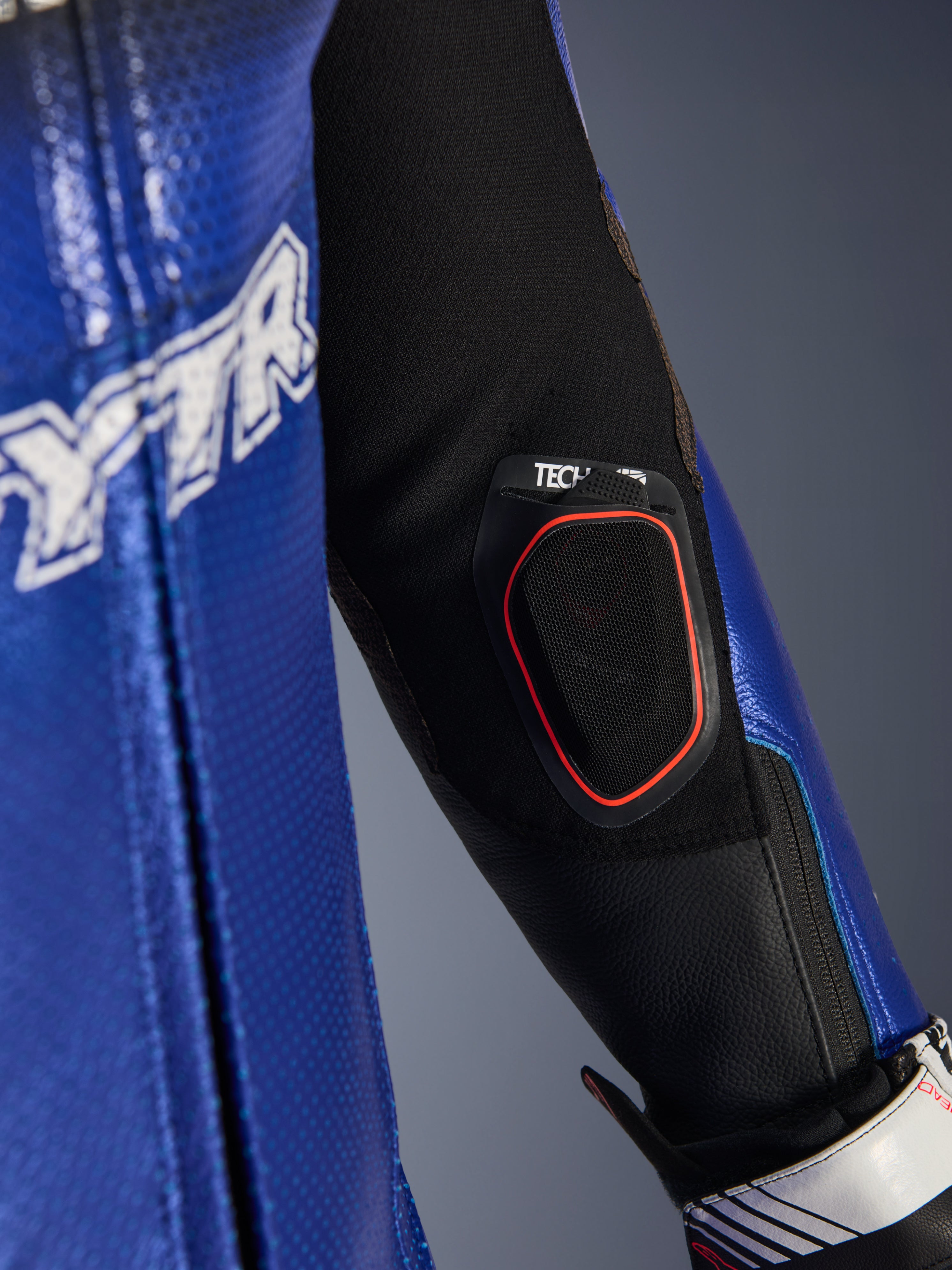 Nahaufnahme des Unterarms des Yamaha GP-R7 Einteiligen Lederanzugs, mit integrierter Tech-Air 10 Bluetooth-Displaytasche mit rotem Rand, metallic-blauem, perforiertem Leder und schwarzen Stretch-Gewebeeinsätzen für Rennperformance.