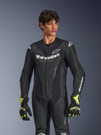 Combinaison en cuir une pièce Alpinestars GP Force V2, noire, logo et marquage Alpinestars blancs, panneaux en cuir perforé pour la ventilation, portée par un modèle masculin avec des gants noirs et jaune fluo, équipement de course moto haute performance