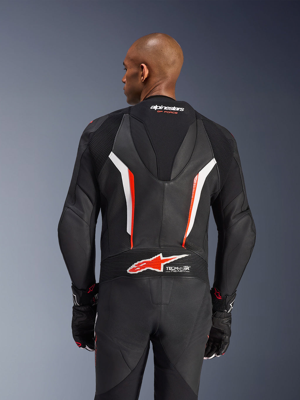 Combinaison en cuir Alpinestars GP Force V2, combinaison de moto 1 pièce, noir, blanc et rouge fluo, vue arrière du haut du corps montrant le cuir perforé et le logo Tech-Air Ready, portée avec des gants noirs et rouges assortis