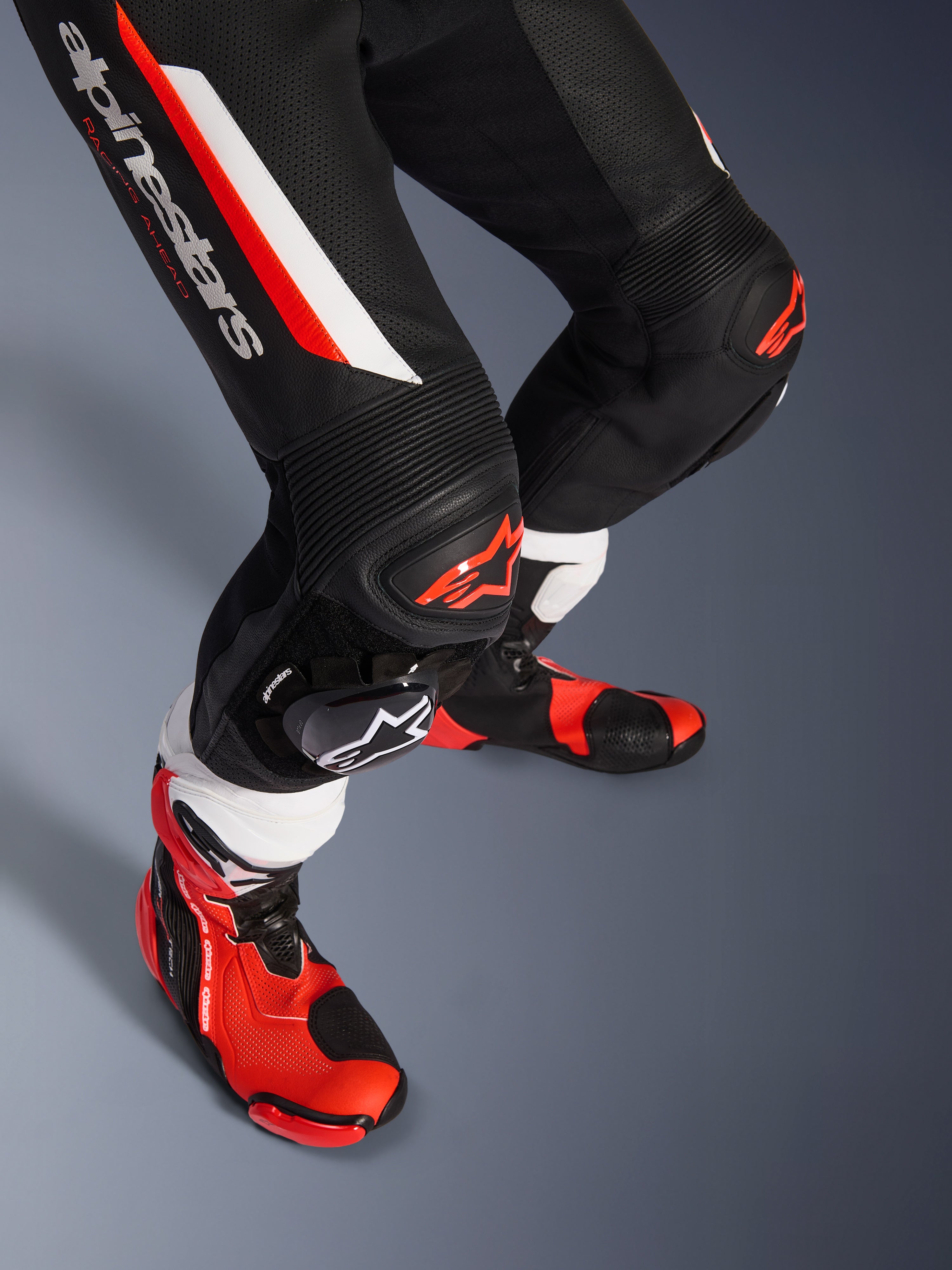 Combinaison en cuir 1 pièce Alpinestars GP Force V2, noir, blanc et rouge fluo, gros plan sur le bas des jambes et les genoux avec protections DFS Lite et sliders remplaçables, associée à des bottes de course professionnelles