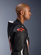 Combinaison en cuir Alpinestars GP Force V2 1 pièce, profil latéral d'un pilote, coloris Noir Blanc Rouge Fluo, mettant en évidence la bosse aérodynamique, les zones en cuir perforé et la protection d'épaule DFS Lite avec le logo Alpinestars rouge